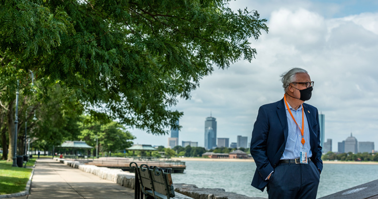 Wearing a mask, Chancellor Marcelo Suárez-Orozco walks UMass Boston's HarborWalk.
